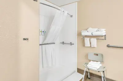 a bathroom with a shower with a mirror and a chair at Comfort Suites Lakewood - Denver in Lakewood