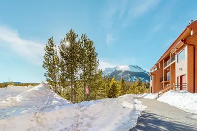 a snow covered road next to a building with a mountain at 2 Bed 2 Bath Apartment in Summit County in Silverthorne