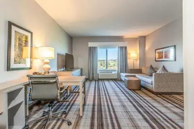 a hotel room with a desk and a living room at Hawthorn Extended Stay by Wyndham Loveland in Johnstown