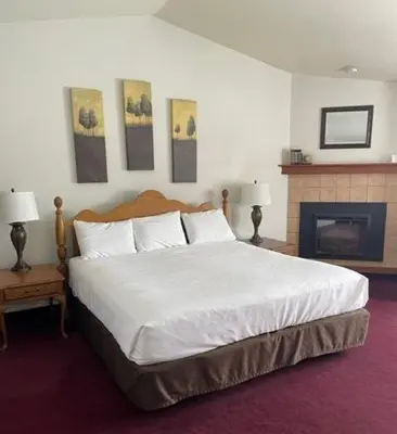 a bedroom with a large white bed and a fireplace at Hilltop Inn Broomfield Denver in Broomfield