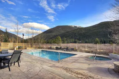a swimming pool with a table and chairs and mountains at 2311 Red Hawk Lodge Condo in Keystone