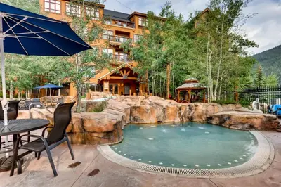 a large pool with a rock wall and a table with an umbrella at 2 Bedroom Colorado Vacation Rental Situated In River Run Village Steps From The Summit Express Gondola in Keystone