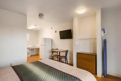 a bedroom with a bed and a desk and a kitchen at HomeTowne Studios by Red Roof Denver - Glendale/ Cherry Creek in Denver