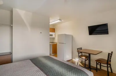a bedroom with a bed and a table and a refrigerator at HomeTowne Studios by Red Roof Denver - Airport/Aurora in Aurora