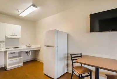 a kitchen with a white refrigerator and a table and a desk at HomeTowne Studios by Red Roof Denver - Airport/Aurora in Aurora