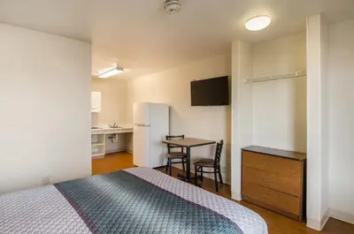 a bedroom with a bed and a table and a refrigerator at HomeTowne Studios by Red Roof Denver - Airport/Aurora in Aurora