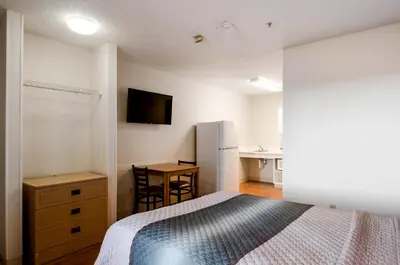 a bedroom with a bed and a desk and a refrigerator at HomeTowne Studios by Red Roof Denver - Thornton in Thornton
