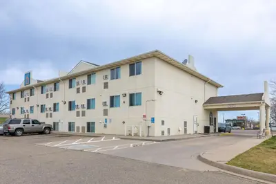 a large white building with a car parked in a parking lot at Motel 6-Fort Lupton, CO in Fort Lupton
