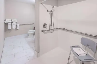 a bathroom with a toilet and a chair in it at Days Inn & Suites by Wyndham Greeley in Greeley
