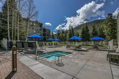 a pool with chairs and blue umbrellas on a patio at Lakeside 1481 by SummitCove Lodging in Keystone