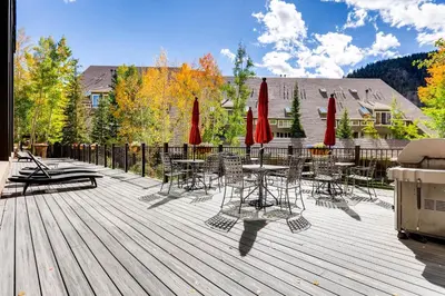 a deck with tables and chairs and red umbrellas at Spacious And Modern 2Br Premier- The Pines- Kids Ski Free Condo in Keystone