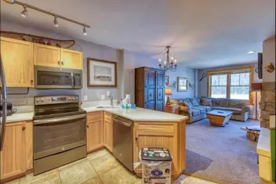 a kitchen with wooden cabinets and a living room at 1 Bedroom Premier Mountain Condo In River Run Village Just A Short Walk To Shopping, Dining, And Skiing in Keystone