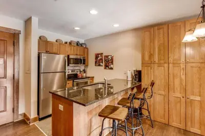 a kitchen with wooden cabinets and a counter with bar stools at Luxury 1 Bedroom Mountain Condo In River Run Village With Expansive Mountain Views And Walking Distance To Ski Slopes in Keystone