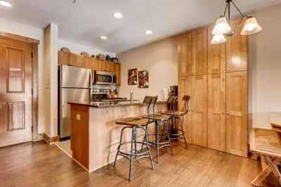 a kitchen with wooden cabinets and a bar with stools at Luxury 1 Bedroom Mountain Condo In River Run Village With Expansive Mountain Views And Walking Distance To Ski Slopes in Keystone