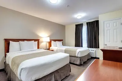 a hotel room with two beds and a desk at Suburban Studios Westminster Denver North in Westminster