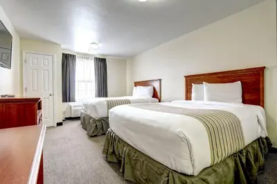 a hotel room with two beds and a desk at Suburban Studios Westminster Denver North in Westminster