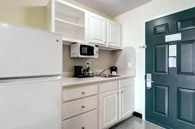 a kitchen with white cabinets and a green door at Suburban Studios Westminster Denver North in Westminster