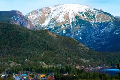 a snow covered mountain with a town in front of a lake at 2 Blocks To Grand Lake Downtown Western Cabin! in Grand Lake