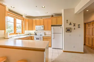 a kitchen with wooden cabinets and a white refrigerator at 7 Mi to National Park Grand Lake Condo with Deck! in Grand Lake