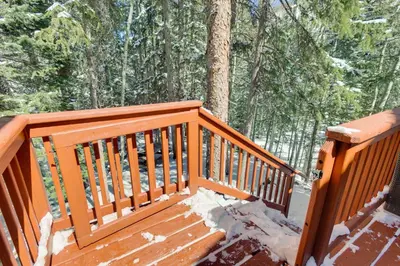 a wooden deck with snow on it in the woods at Idaho Springs Cabin with Hot Tub on Half Acre! in Idaho Springs