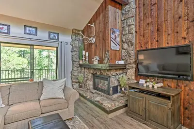 a living room with a stone wall with a flat screen tv at Condo with Pool and Hot Tub - Walk to DT Winter Park! in Winter Park