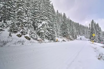 a snow covered road with trees on the side at Ski-InandSki-Out Winter Park Condo with Hot Tub Access in Winter Park