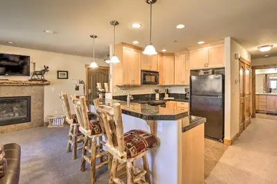 a kitchen with wooden cabinets and a island with bar chairs at Peaceful Fraser Condo with Patio - by Hiking Trails! in Fraser