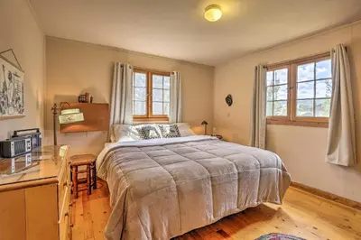 a bedroom with a bed and a desk and two windows at Walk to Grand Lake Historic Dtwn Cabin! in Grand Lake