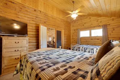 a log cabin bedroom with two beds and a flat screen tv at Picturesque Log Cabin in Estes Park 9 Mi to RMNP in Estes Park