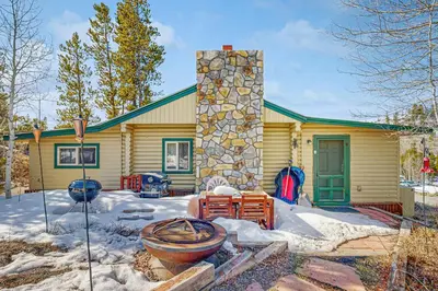 a house with a stone chimney in the snow at Grand Lake Cabin Escape in Grand Lake