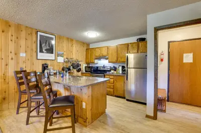a kitchen with wooden cabinets and a counter with chairs at Mtn Condo with Ski Locker and Pools - 3 Mi to Resort! in Winter Park