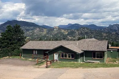 a green house with mountains in the background at Rocky Mountain Retreat 1A by Rocky Mountain Resorts in Estes Park