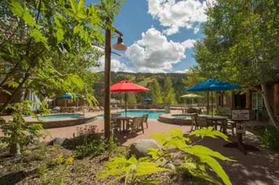 a patio with tables and umbrellas and a swimming pool at Premier 2 Bedroom Mountain Condo In River Run Village With Expansive Mountain Views And Walking Distance To Ski Slopes in Keystone