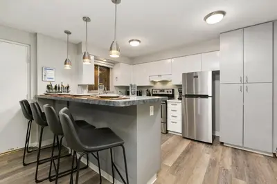 a kitchen with white cabinets and a large island with bar stools at Stunning Downtown Condo - 5 min walk to Old Town! in Fort Collins