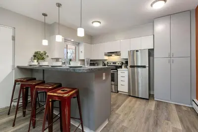 a kitchen with white cabinets and bar stools at Old Town Condo by Library Park Walk Everywhere! in Fort Collins