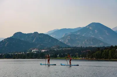 two people are on paddle boards in the water at Rocky Mountain Escape - Steps to Lake Estes, Jacuzzi, Close to Downtown Estes in Estes Park