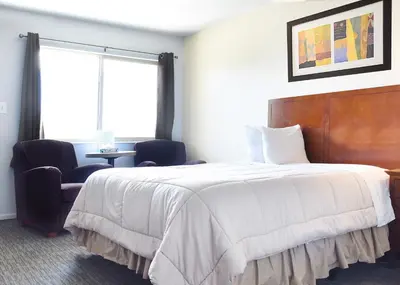 a bedroom with a large white bed and a chair at GREELEY UNIVERSITY INN/ GREELEY INN in Greeley