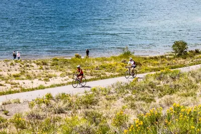 two people riding bikes on a path near the water at River Run Townhomes by Summit County Mountain Retreats in Keystone