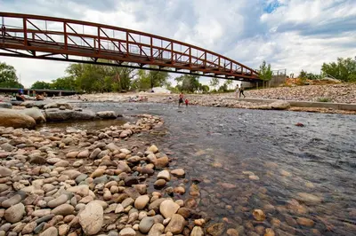 a bridge over a river with rocks in the water at Old Town Modern New Build - Rooftop Spa with Mtn Views! in Fort Collins