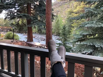 a person with their feet on a railing looking out at a forest at Riverfront Mountain Cottage Retreat in Estes Park