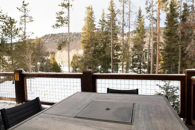 a wooden table on a deck with a view of trees at The Seasons 1818 condo in Keystone