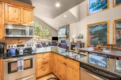 a kitchen with wooden cabinets and a living room at River Rock Retreat -- EV #6032 condo in Estes Park