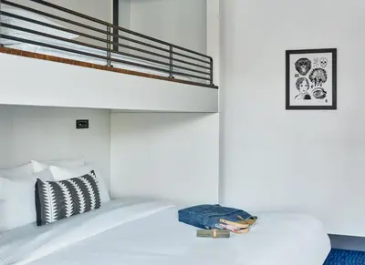 a white bedroom with a bunk bed with a pillow and a suitcase at The Maven Hotel at Dairy Block in Denver