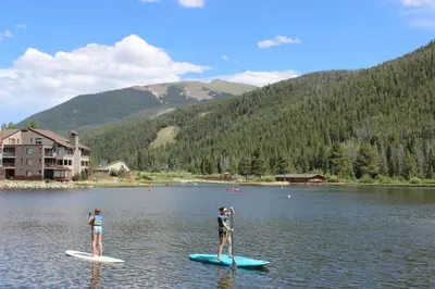 two people are standing on paddle boards in the water at Lakeside 1476 by SummitCove Lodging in Keystone