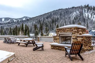 a patio with a stone fireplace and tables and chairs at Ski-In Ski-Out Modern Mountain Condo in Winter Park