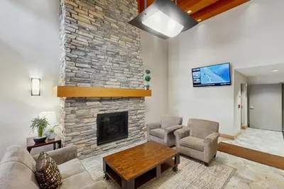 a living room with a stone fireplace and a tv at Ski-In Ski-Out Modern Mountain Condo in Winter Park