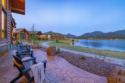 a group of chairs sitting on a patio next to a lake at Chic Lakefront Cabin - Unbeatable Views! Jacuzzi, Two Patios, Indoor/Outdoor Fireplace in Estes Park