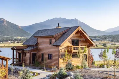 a log home with mountains in the background at Private Lakefront Cabin - Two Large Patios, Jacuzzi, Indoor/Outdoor Fireplace in Estes Park