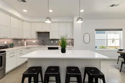 a kitchen with a white island with four stools at Gorgeous Townhome Steps from the Brewery District! in Fort Collins