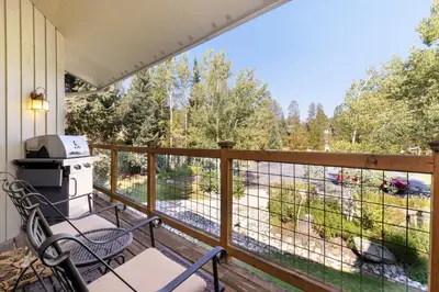 a balcony with a grill and chairs and a view of the woods at 1196 Flying Dutchman condo in Keystone